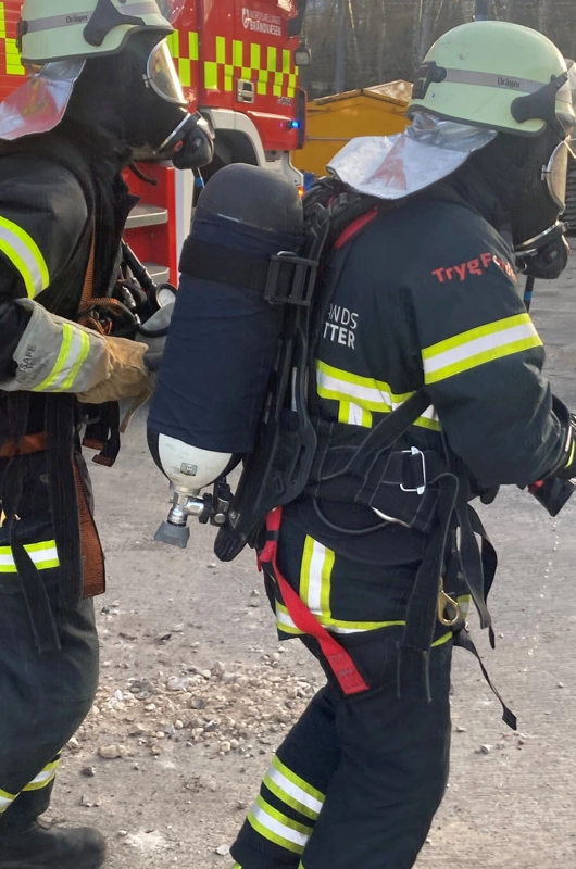 2 brandkadetter i fuld uniform. De er parat til røgdykning med hjelme, masker og iltmasker på ryggen.